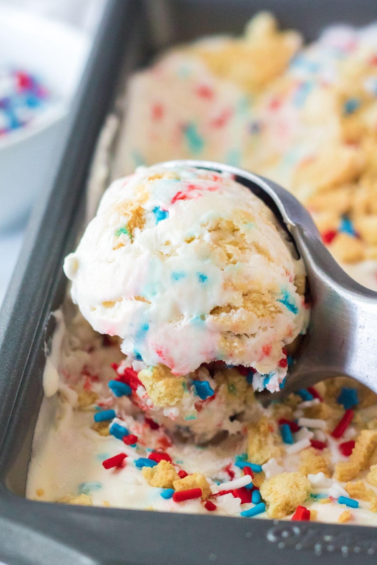 ice cream scoop scooping vanilla ice cream with red, white and blue sprinkles in it