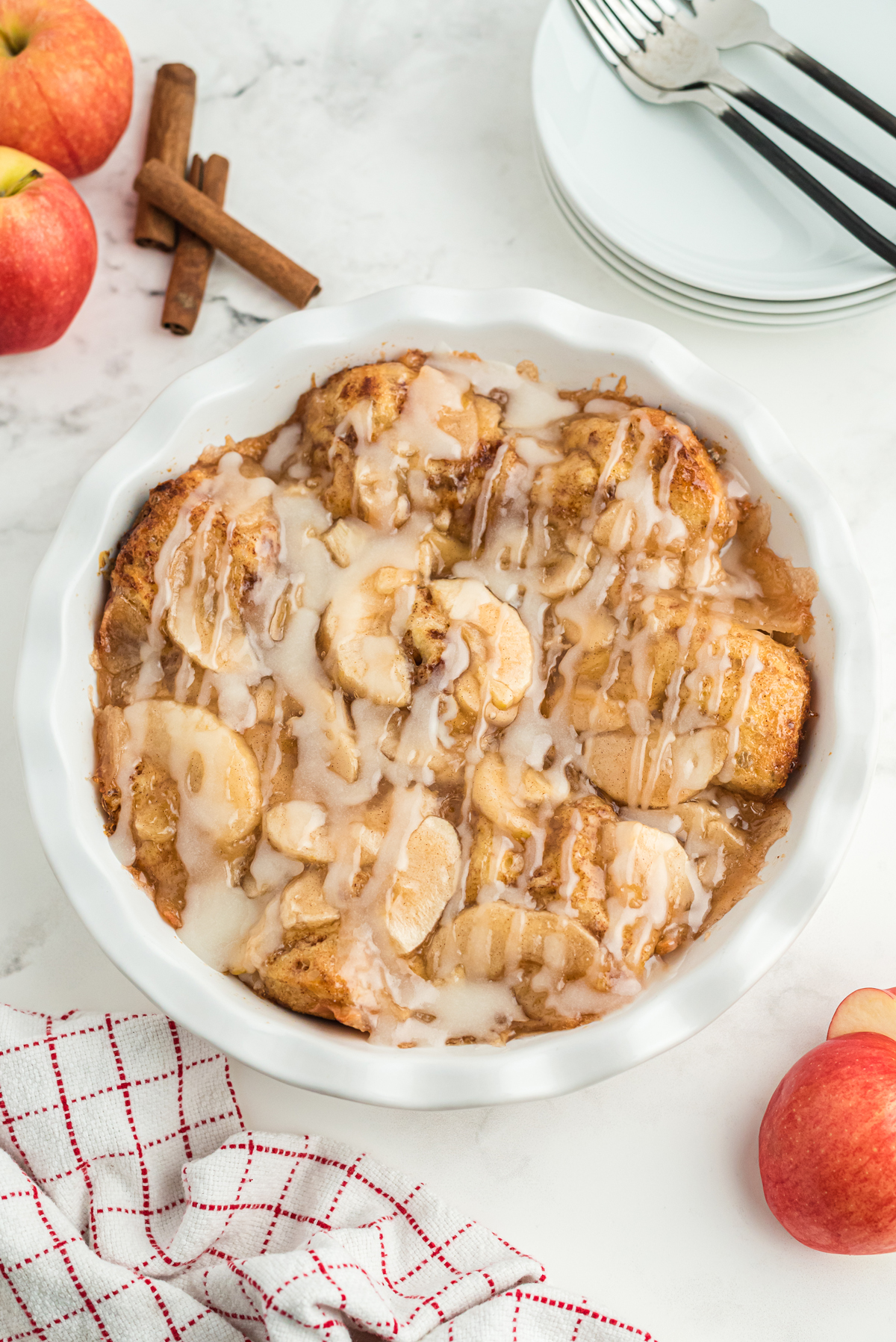 Top view of cinnamon Roll Apple Bake in a white pie dish with frosting drizzled over it.