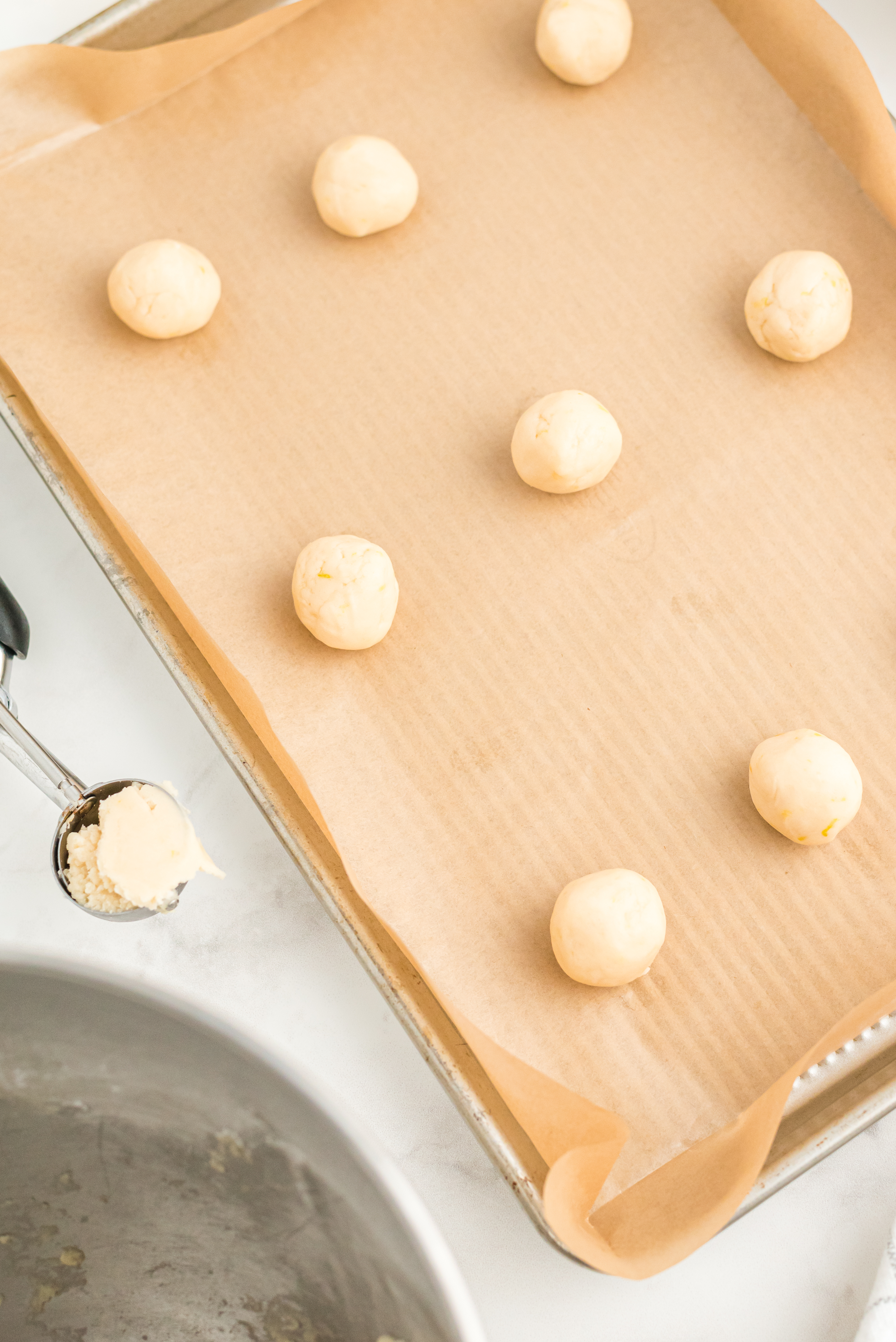 Baking skeet lined with parchment paper covered with small balls of cookie dough in rows of threes. 