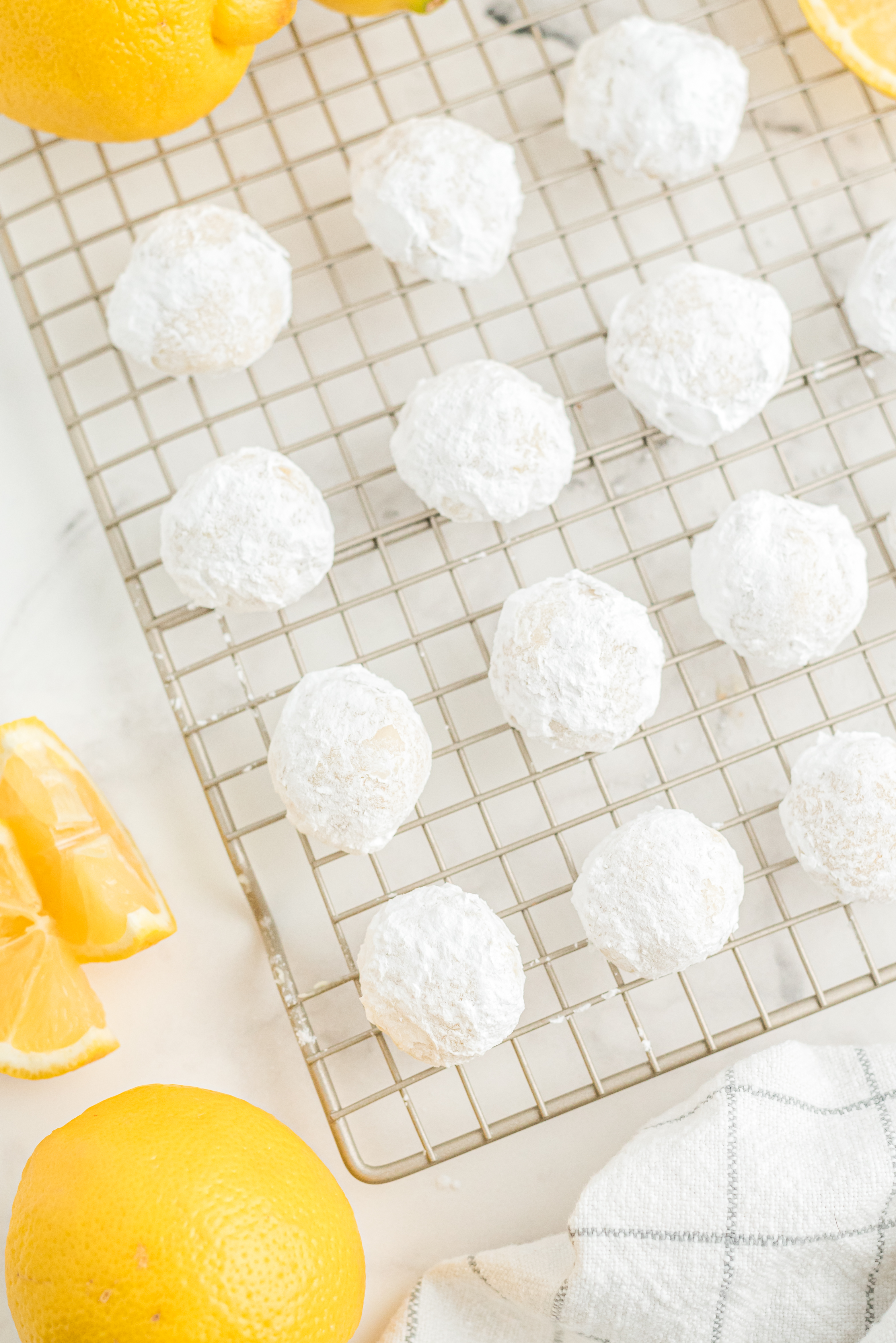 Wire rack on a worktop filled with neat rows of round Lemon Cooler Cookies covered in powdered sugar.