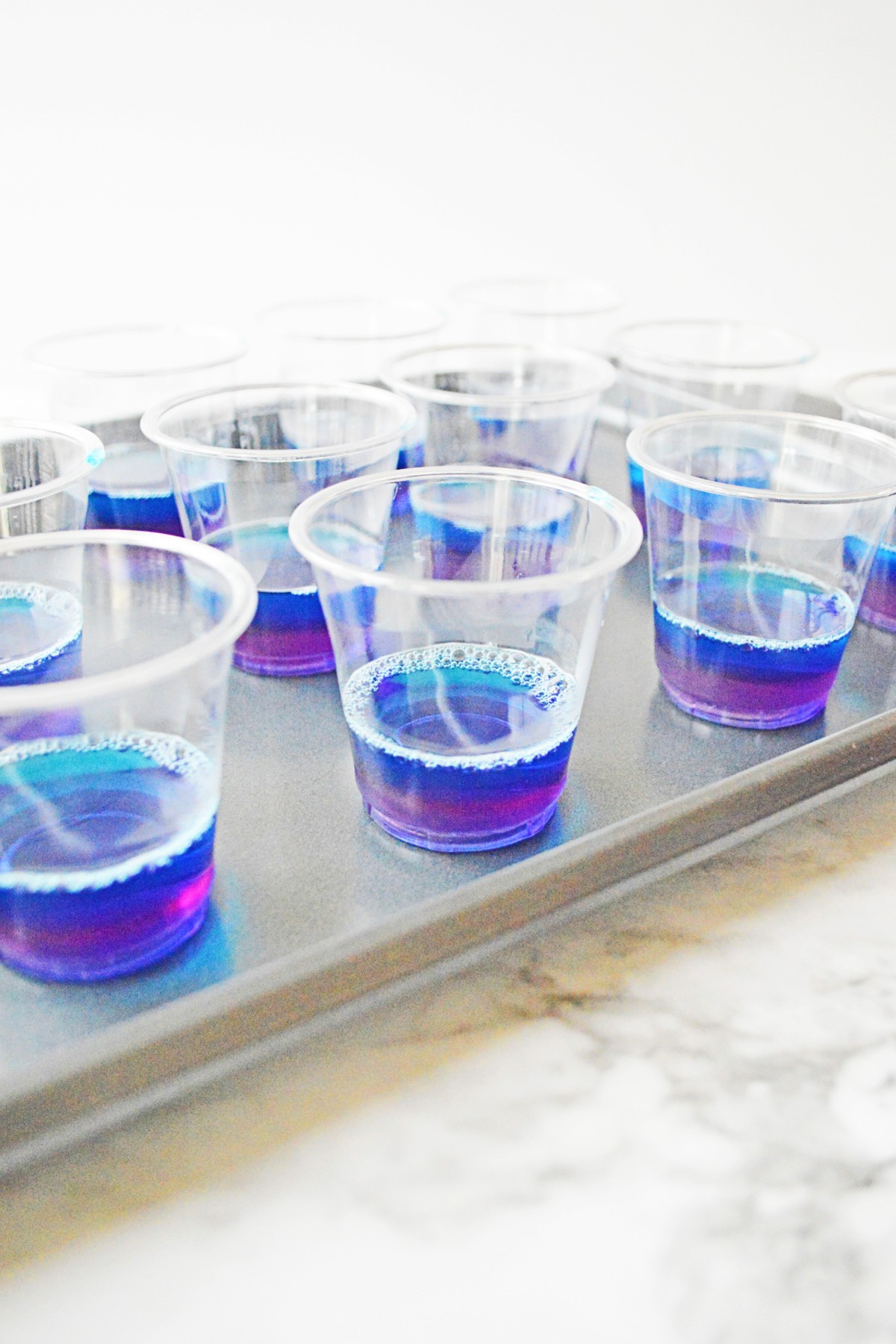 Close up of tray filled with small transparent cups with a blue layer of jello in the bottom
