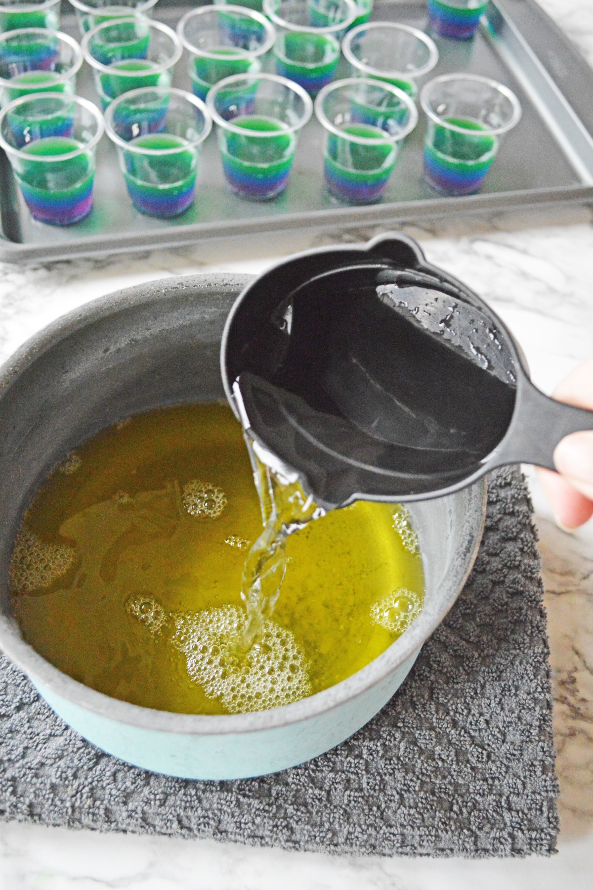 A white bowl with yellow liquid on the bottom with a measuring cup in mid-air pouring clear liquid into it. 