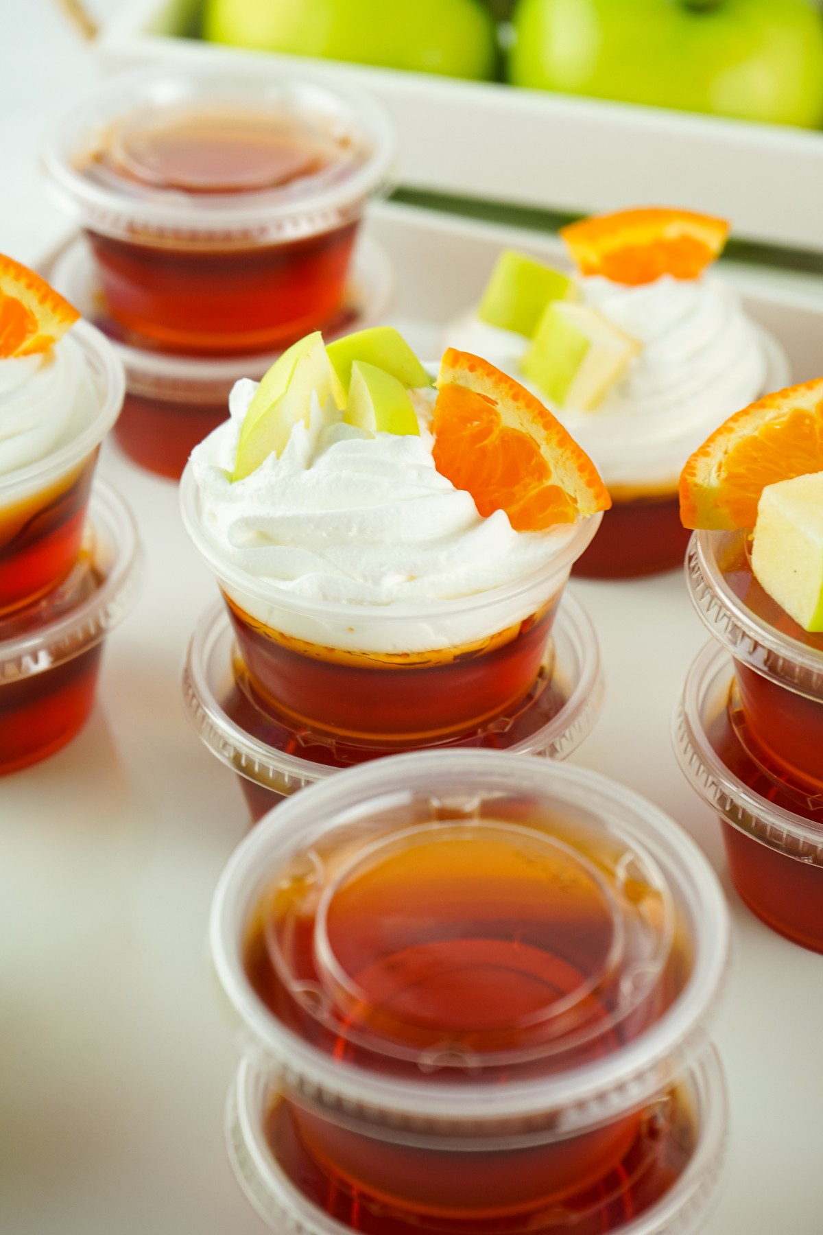 Sangria Jello Shots are stacked on each other, the ones on top are topped with whipped cream and small slices of orange and apple. 