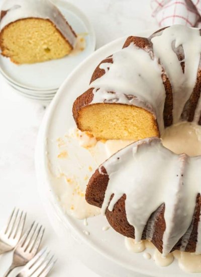 Bundt cake on a white cake plate with a slice cut out of it, and a slice of cake on a white plate sitting next to it.