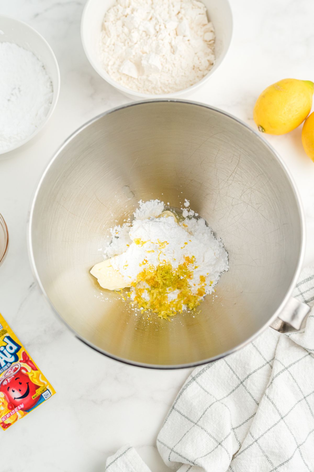 Metal mixing bowl with powdered sugar, butter and lemon juice in the bottom, unmixed. 