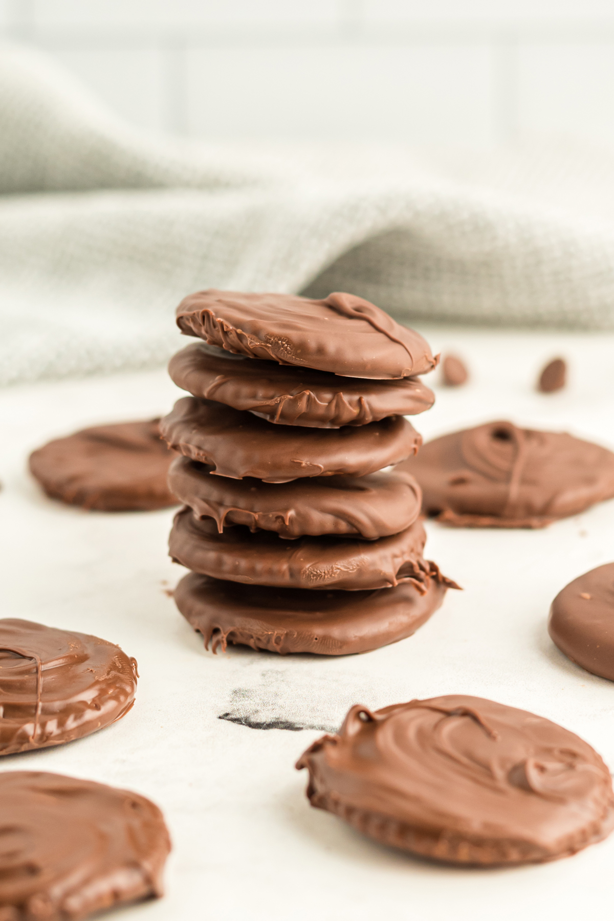Thin Mints Ritz Cookies piled up on a white worktop with single Thin Mints next to them. 