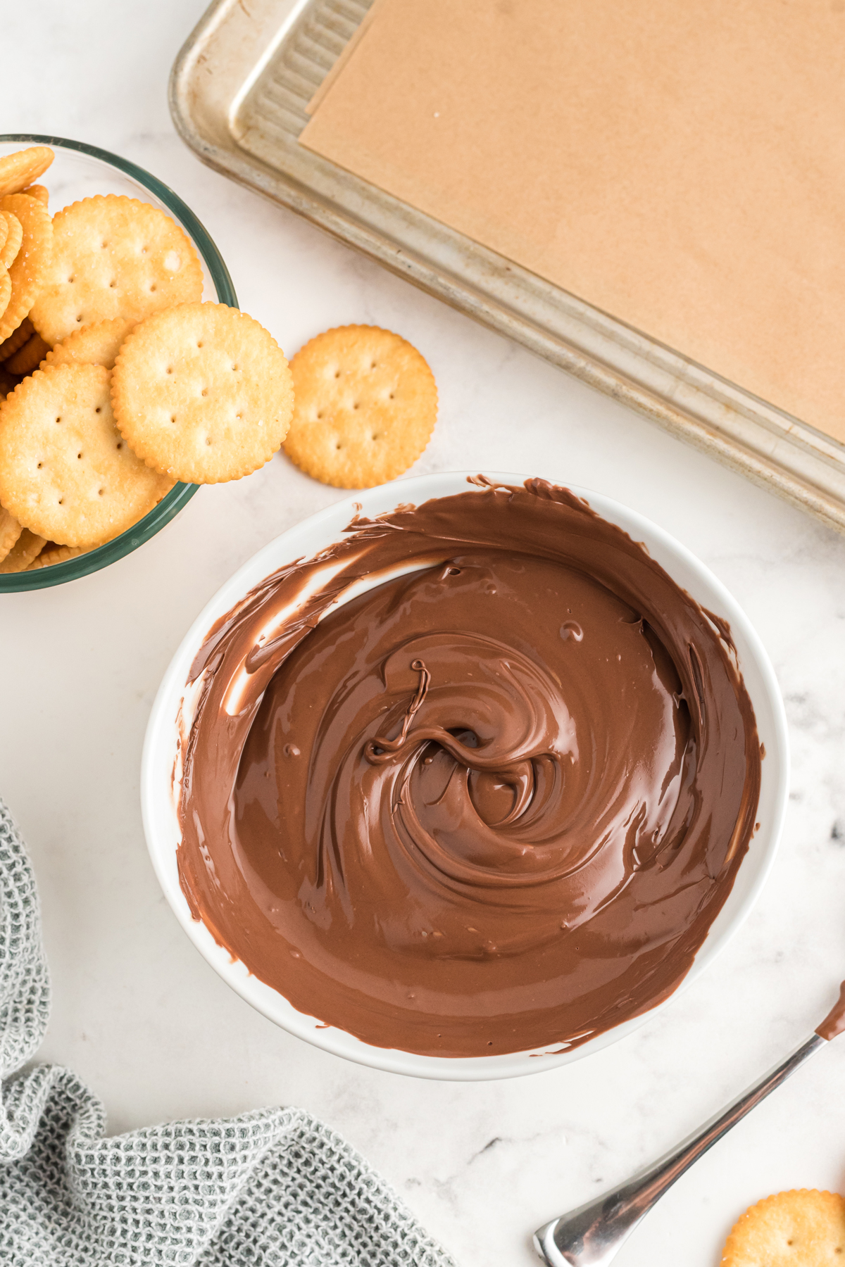 First step in preparing Ritz Cracker Thin Mints is to melt the chocolate. A baking tray lined with parchment paper and crackers can be seen in the corner of the picture. 
