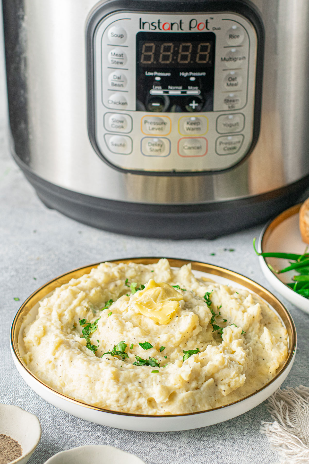 A plate of Instant Pot Garlic Mashed Potatoes with ingredients on the background. 