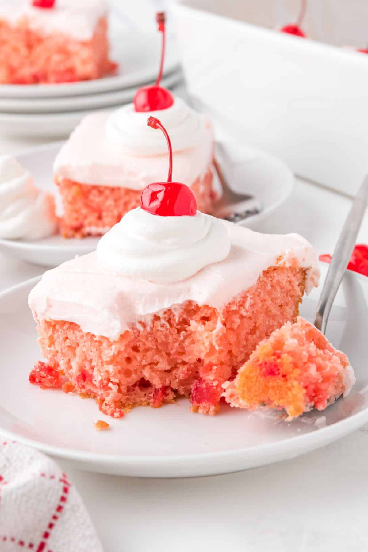 square slices of cherry chip cake with pink frosting and a cherry on top