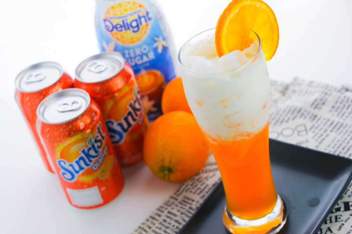 orange creamsicle soda with white on top and an orange slice next to cans of orange soda and oranges