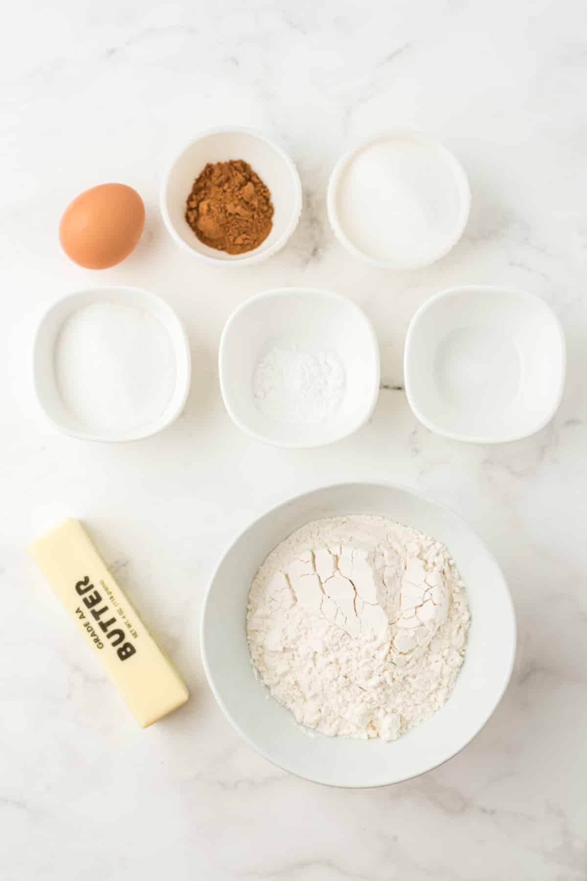 Ingredients for Pumpkin Snickerdoodles recipe on a white counter. These are the following: ½ Cup Butter – softened , ½ Cup Brown Sugar, ¼ Cup White Sugar , 1/3 Cup Pumpkin Puree, 1 tsp Vanilla, 1 ½ Cup Flour , 1 ½ tsp Pumpkin Spice, 1 tsp Cream of Tartar, ½ tsp Baking Soda, ¼ tsp Salt For rolling the cookie the ingredients are: ¼ Cup Sugar, 2 tsp Pumpkin Spice