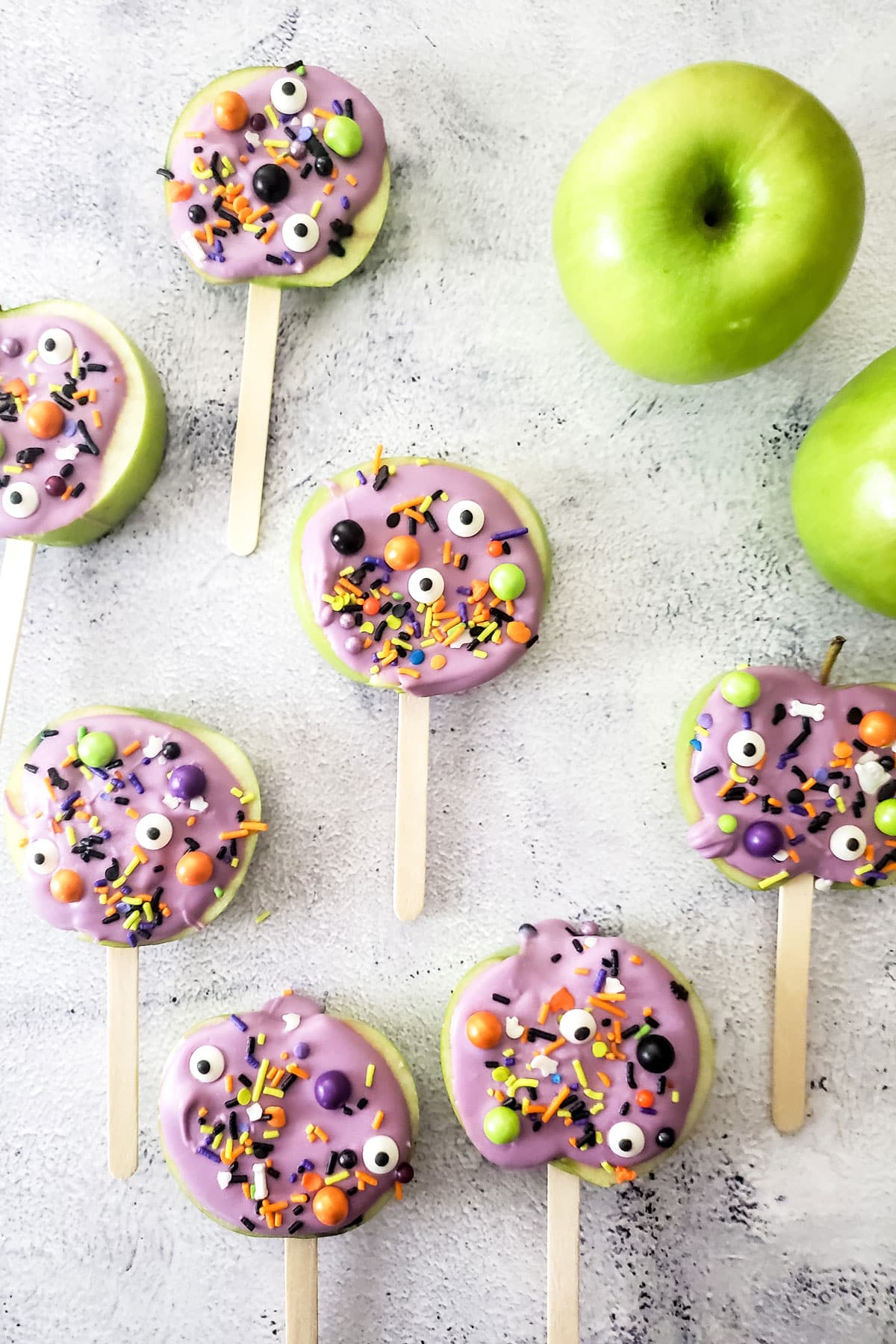 apple slices on popsicle sticks with purple chocolate and Halloween sprinkles