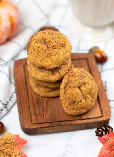A pile of Pumpkin Snickerdoodles cookies on a wooden chopping board with decorations on the side