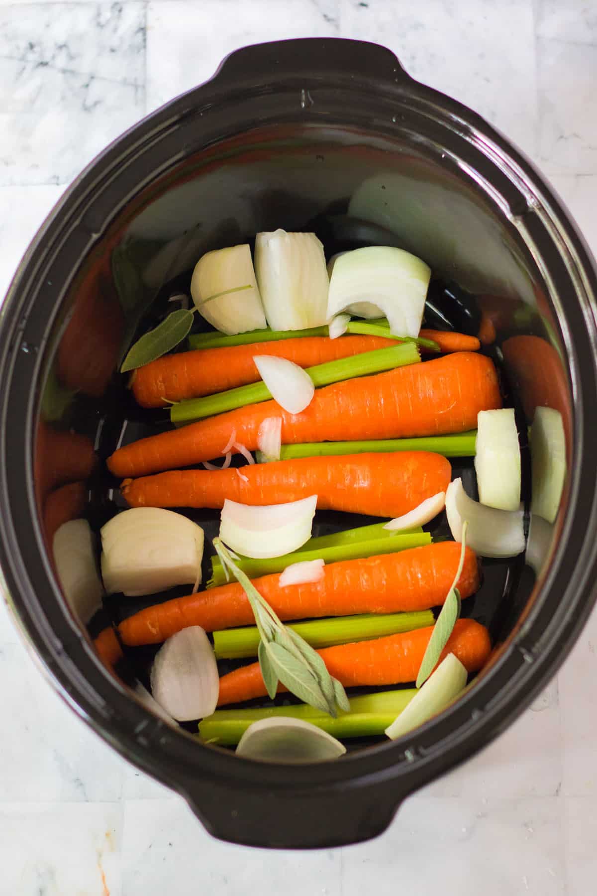 chopped onion, with celery stalks and carrots in the bottom of crockpot