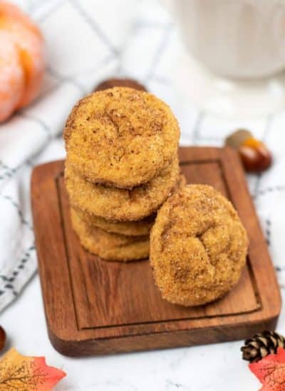 A pile of Pumpkin Snickerdoodles cookies on a wooden chopping board with decorations on the side