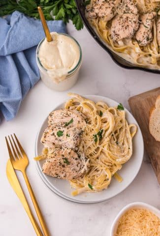Copycat Olive Garden Alfredo Sauce recipe on a white plate with eating utensils on the side.