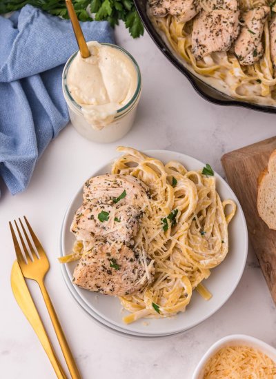 Copycat Olive Garden Alfredo Sauce recipe on a white plate with eating utensils on the side.