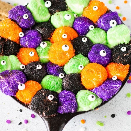 black, green purple and orange marshmallows with candy eyes in cast iron pan