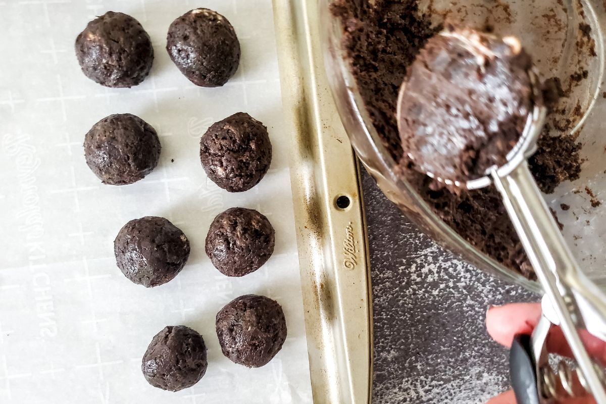 small cookie scoop scooping balls of truffle dough onto baking sheet lined with wax paper