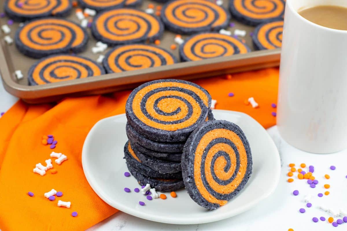 cup of coffee with a plate of black and orange swirl cookies
