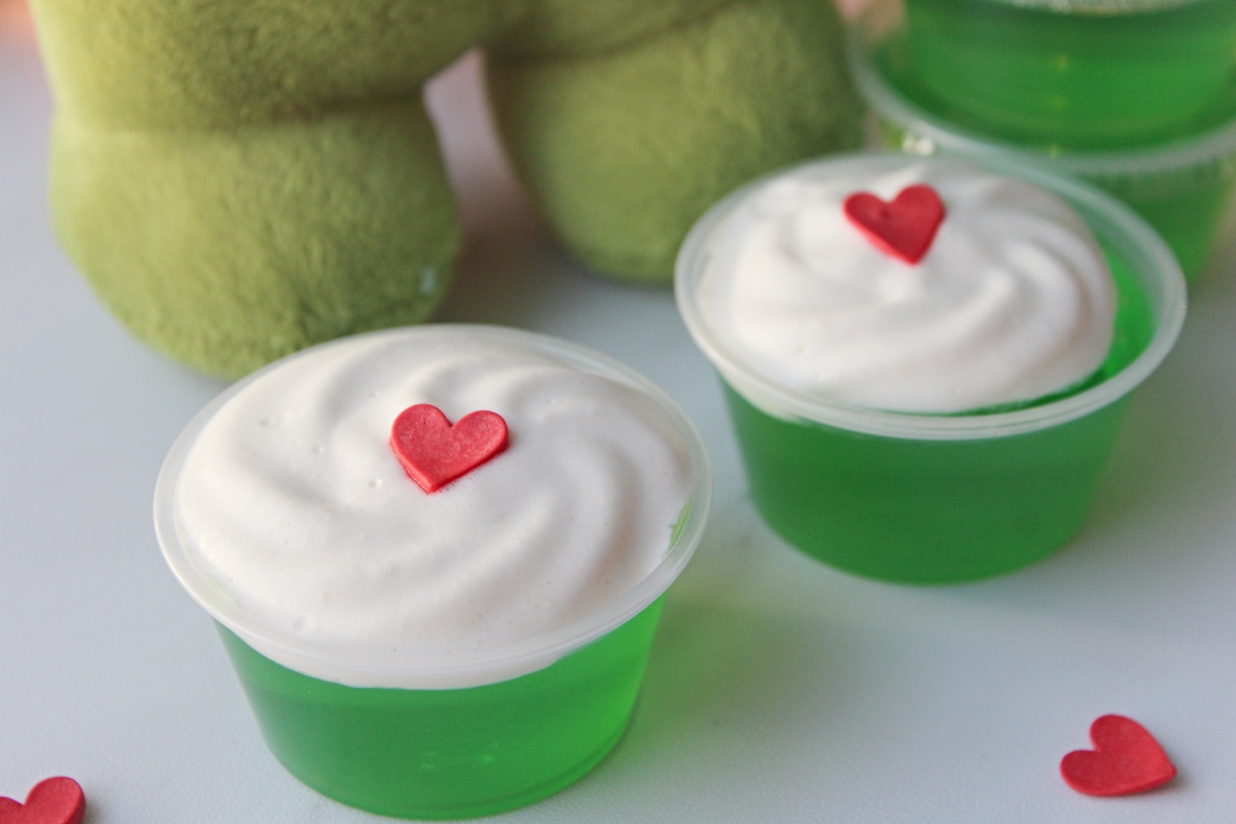 Grinch Jello Shots with heart sprinkles and Grinch character at the back.