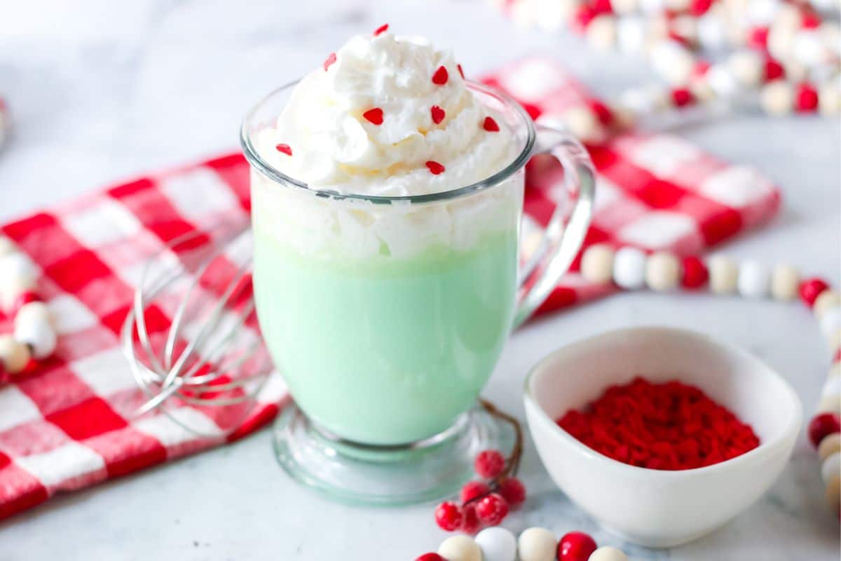 green hot chocolate in clear glass with whipped cream and red heart sprinkles on top