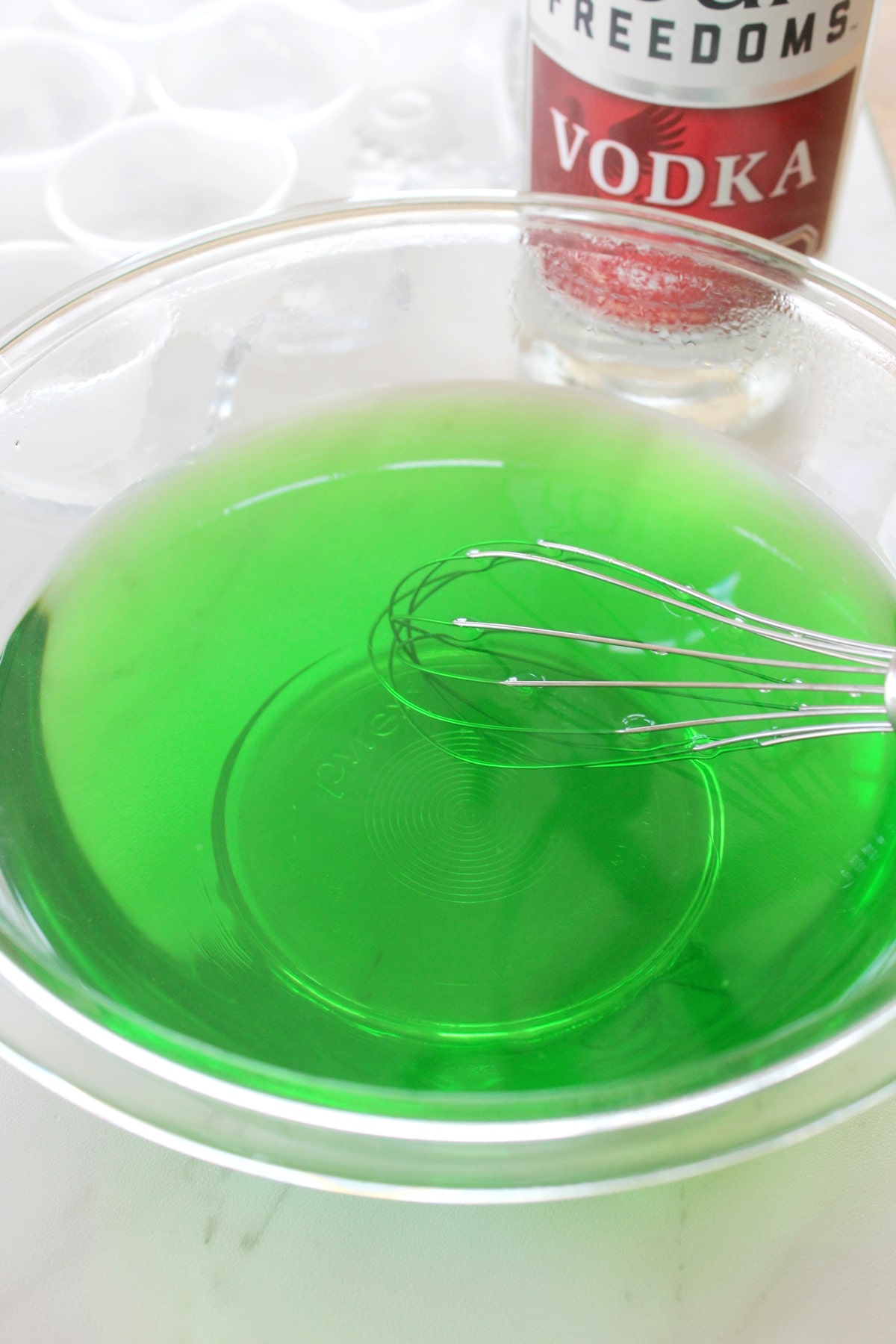 Mixing green jello in a bowl of boiling water until it dissolves.