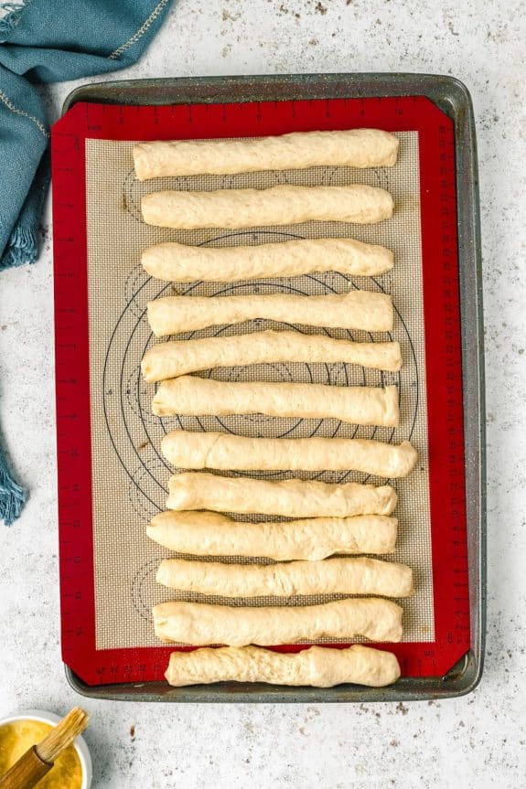 raw dough rolled into breadsticks on baking sheet