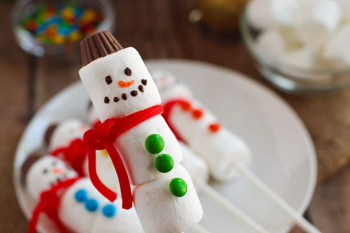 closeup of one marshmallow snowman on popsicle stick with green buttons and a red scarf