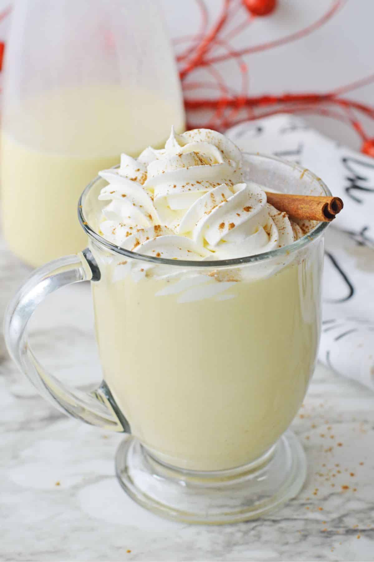 clear glass with egg nog and whipped cream and cinnamon stick