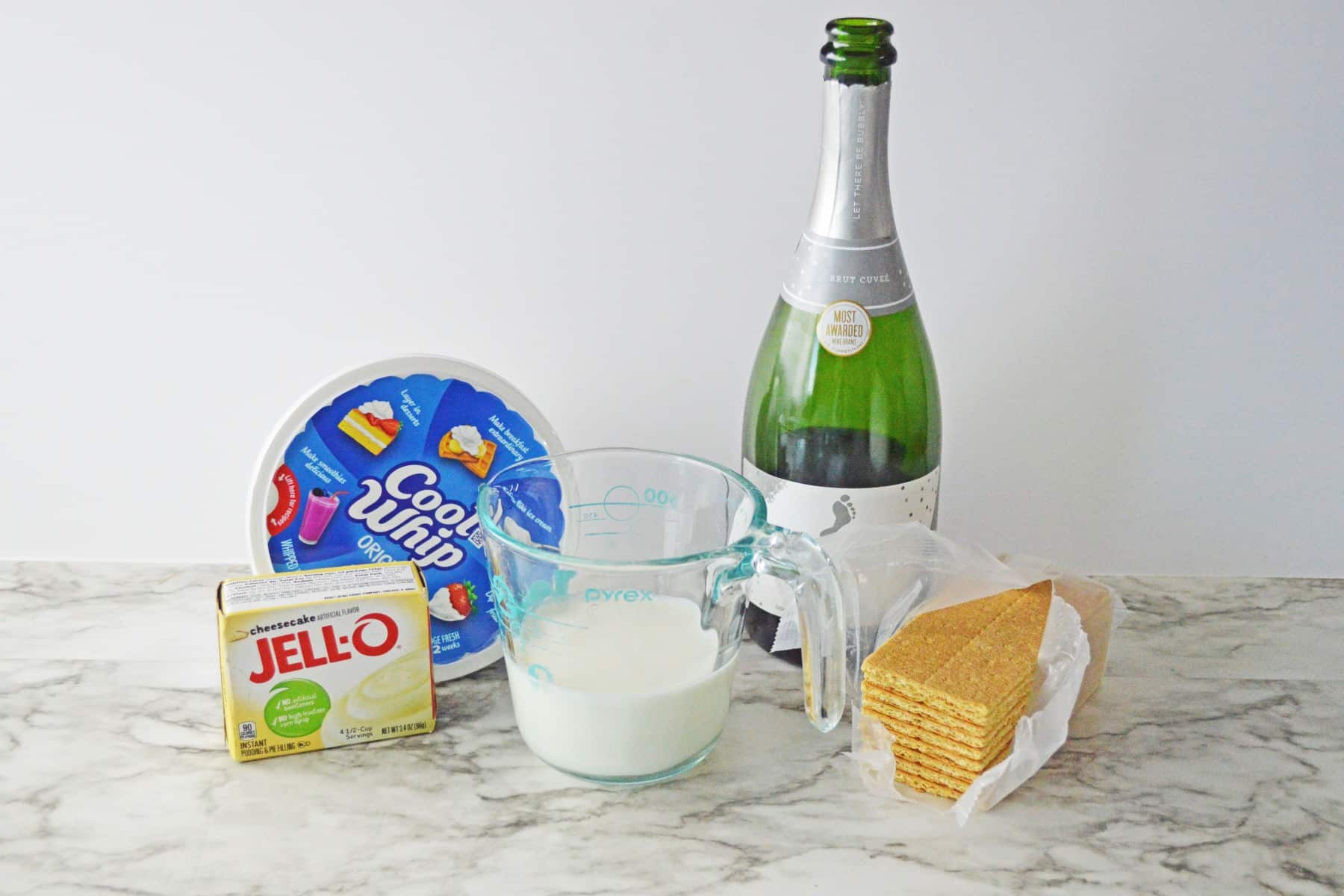 Ingredients for Champagne Cheesecake Shooters are the following:1 (3 oz.) box of instant cheesecake pudding, 1 cup milk, 1 cup champagne, 1 ½ cups cool whip whipped topping, 6 graham crackers, and 12 firework poof cocktail picks