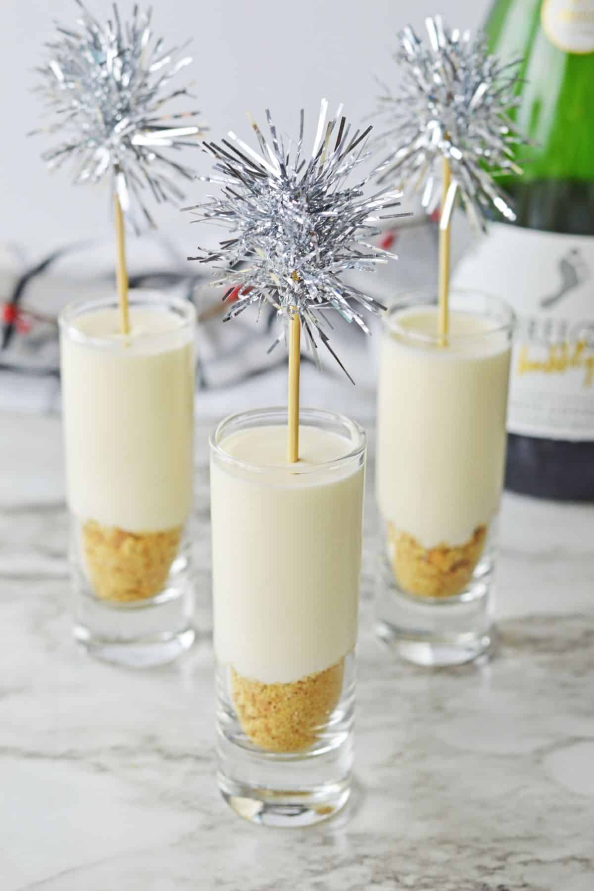 three tall shot glasses with cheesecake inside and silver mini pompoms on top