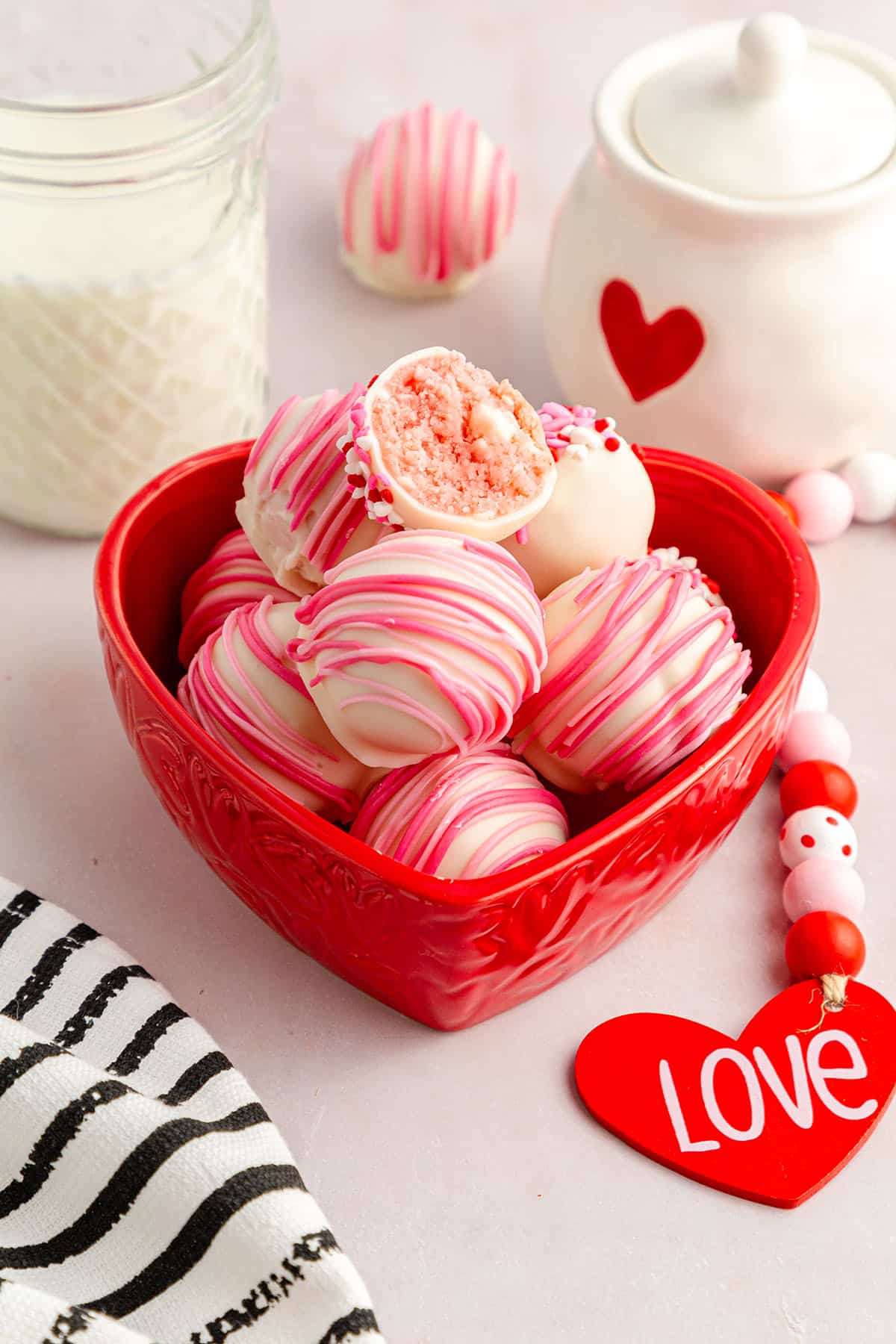 Beautifully drizzled strawberry cheesecake balls placed in a red heart jar