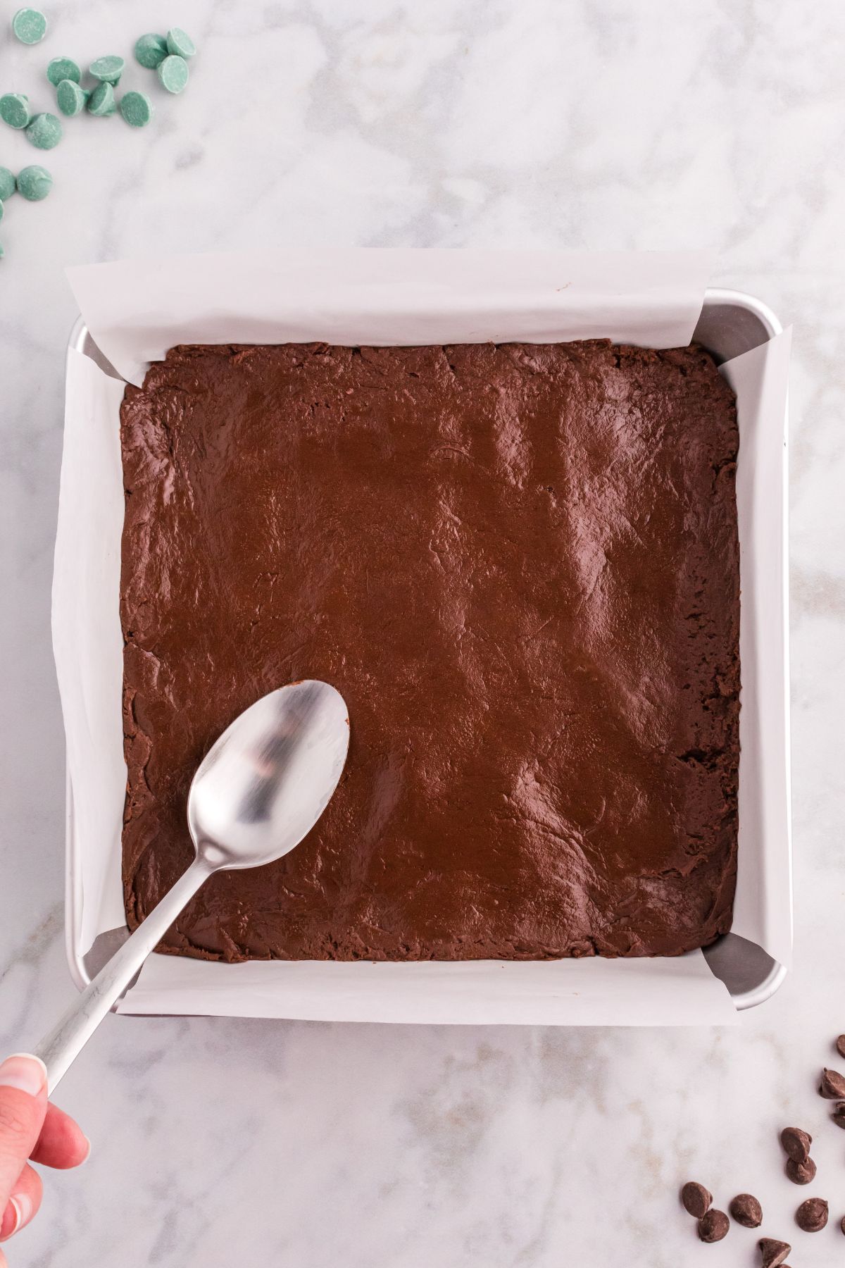 chocolate fudge mixture in bottom of square pan with spoon patting it down