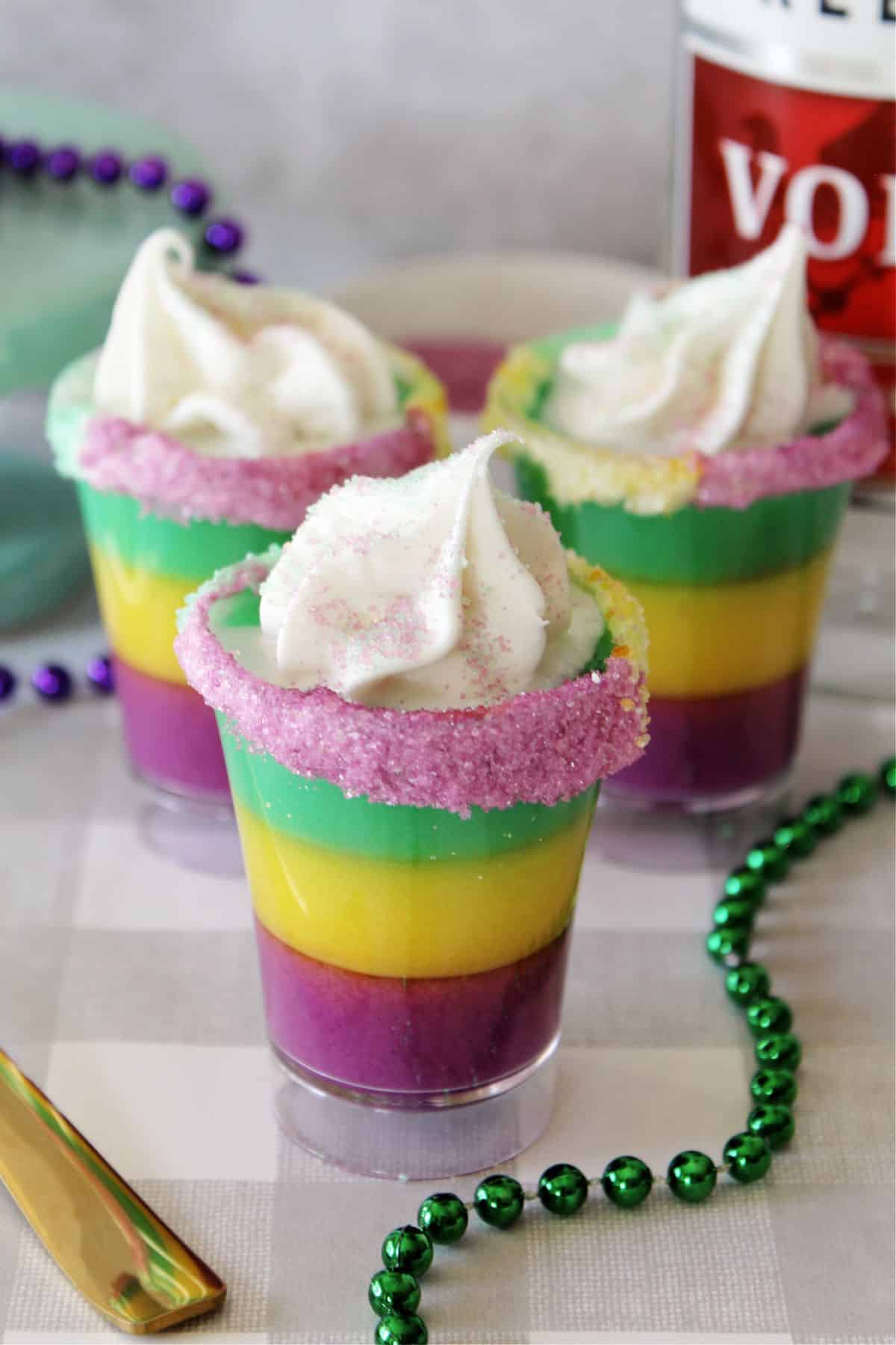 purple, yellow, and green layered pudding shots with whipped cream and purple sanding sugar