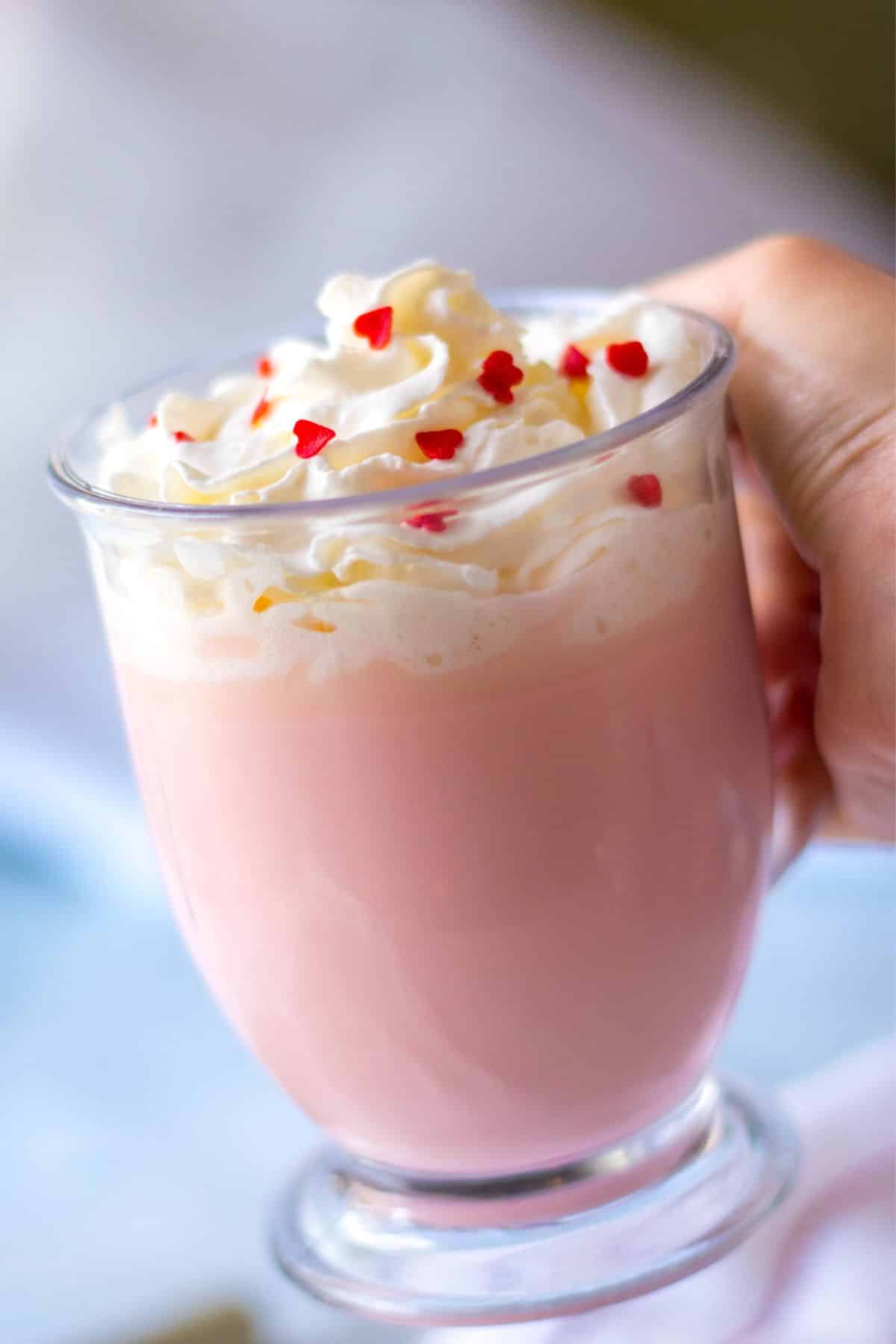 clear mug with pink hot chocolate with whipped cream and red heart sprinkles