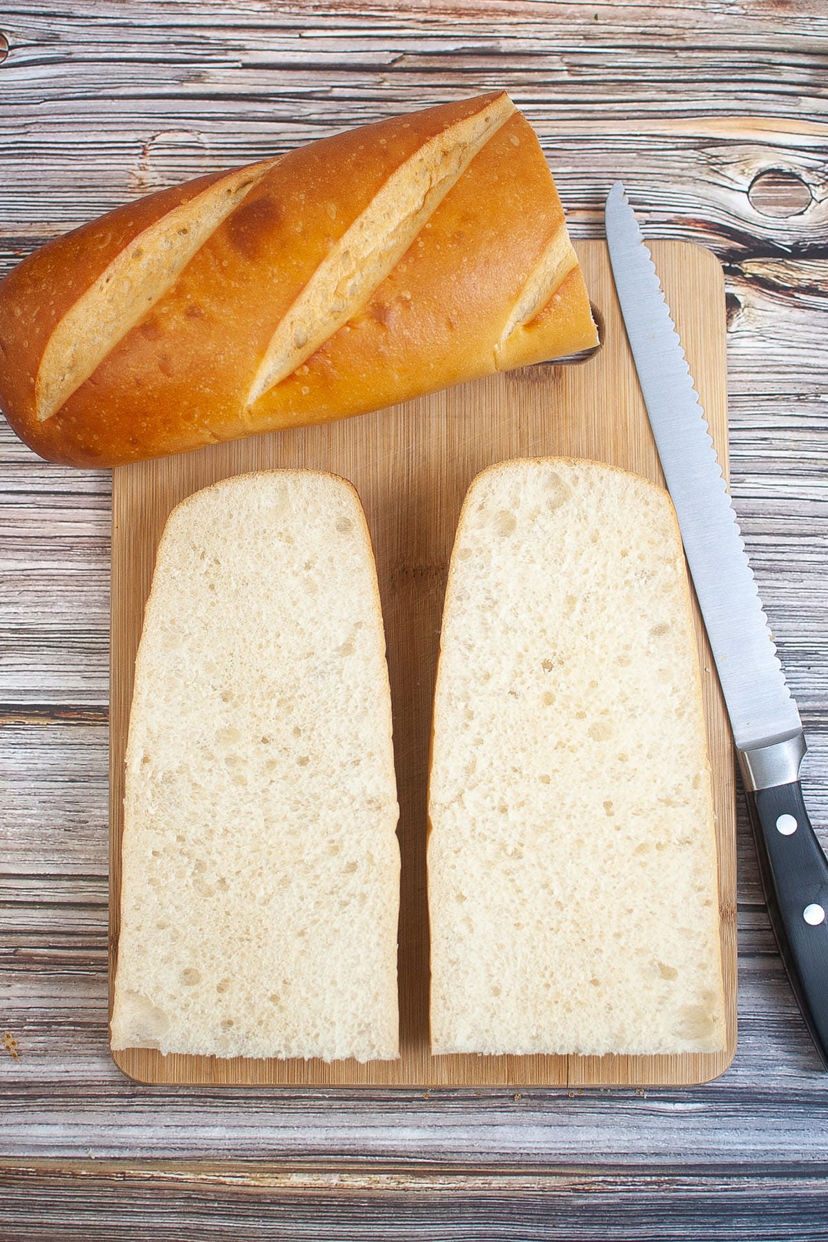 French bread cut in half lengthwise in wood chopping board and bread knife