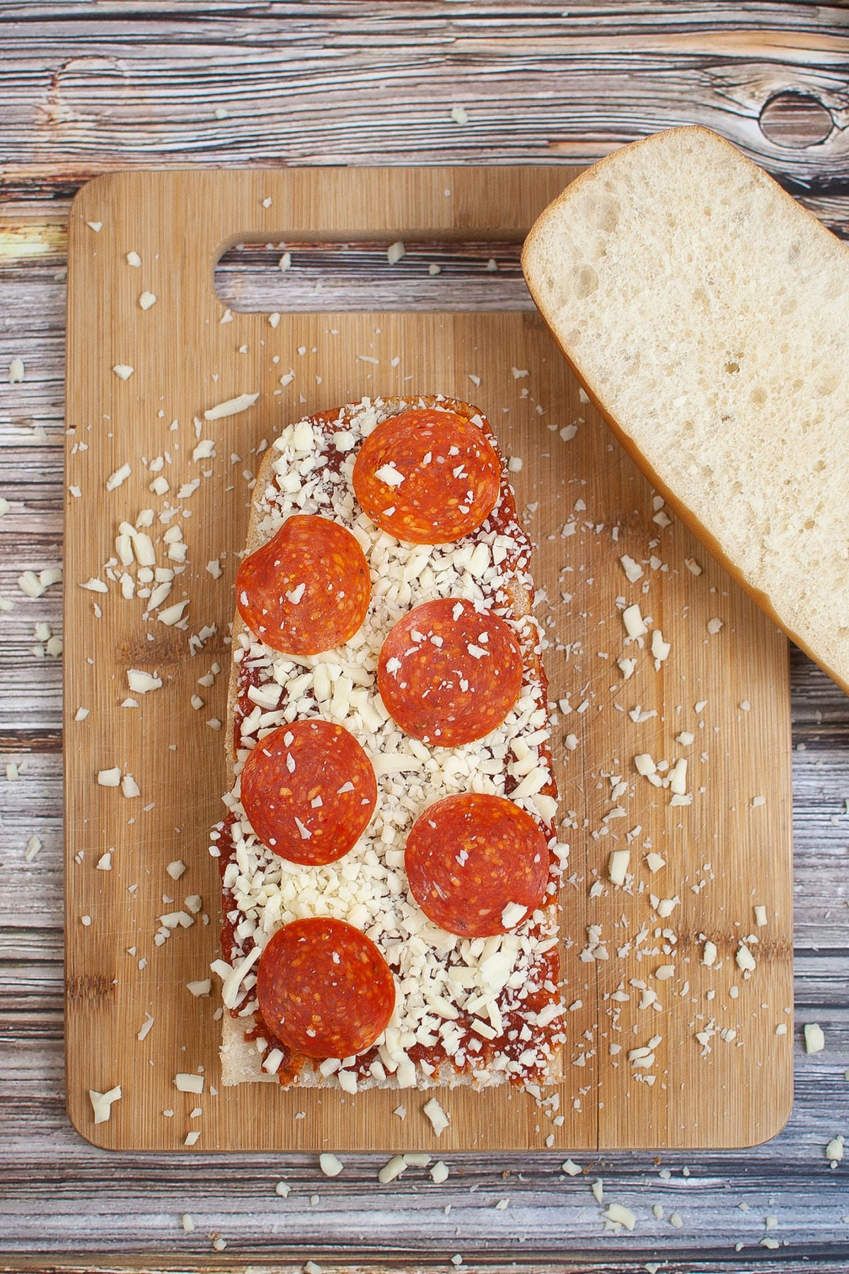 A slice bread with tomato sauce mixture topped with cheese and pepperoni in a wooden chopping board