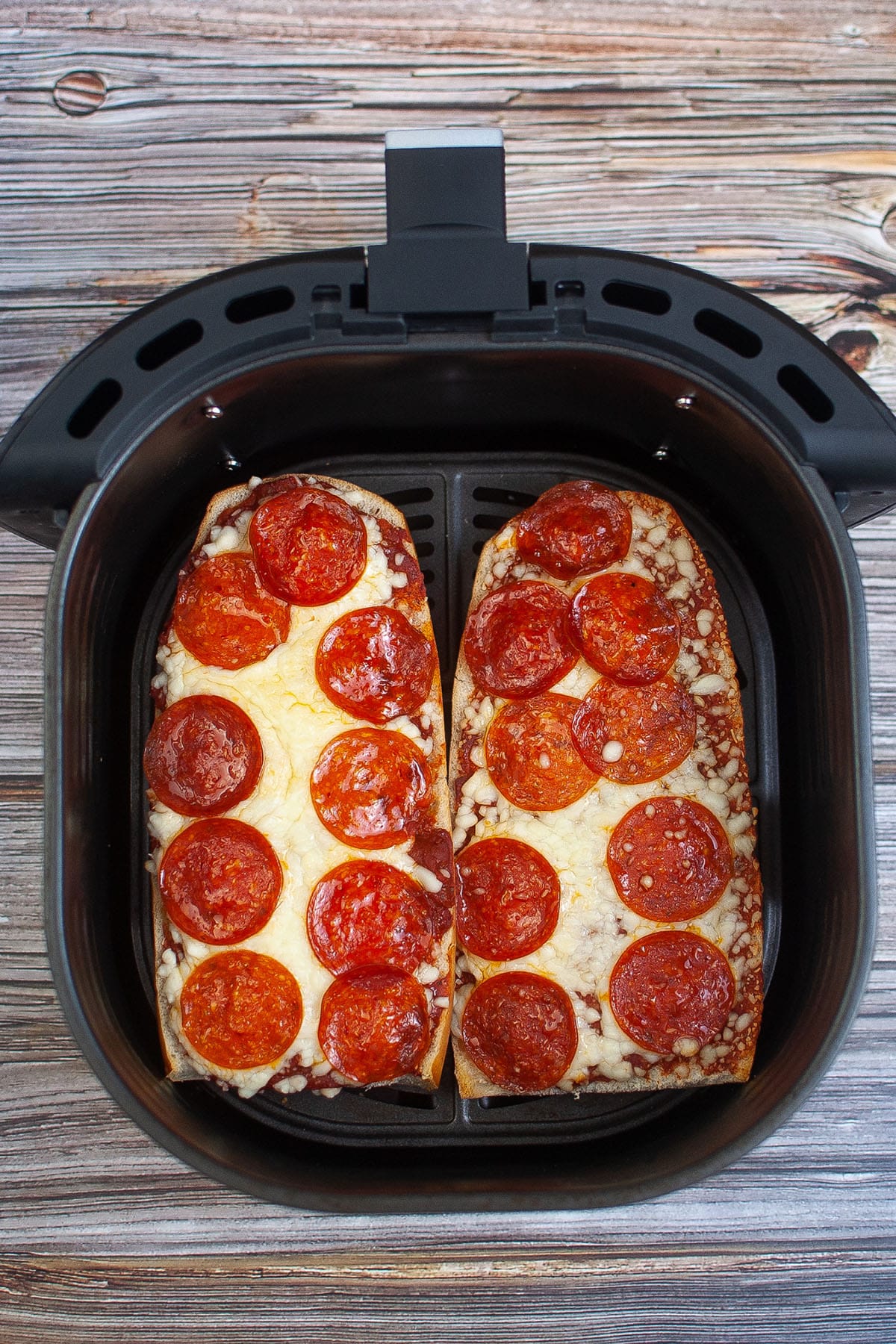 Black air fryer basket containing a cooked pepperoni pizza