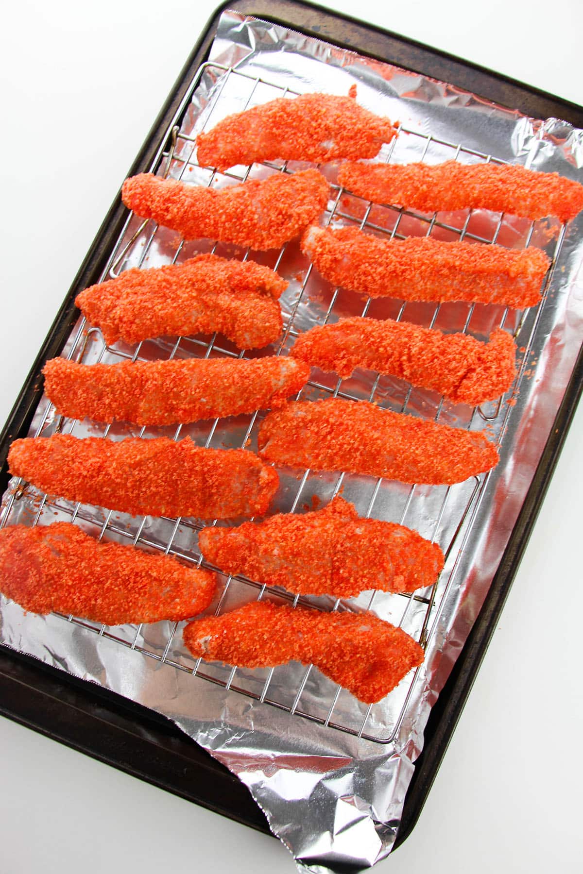 An ovenproof rack with an aluminum foil-lined baking sheet with the hot Cheeto chicken tender