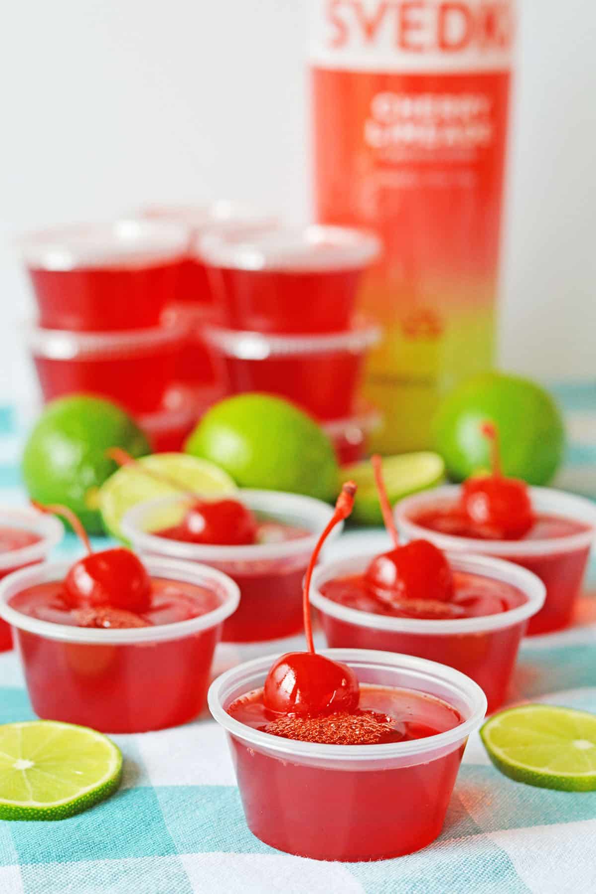 Cherry Jello shots in cups with luscious cherries on top and lime decorations on the table