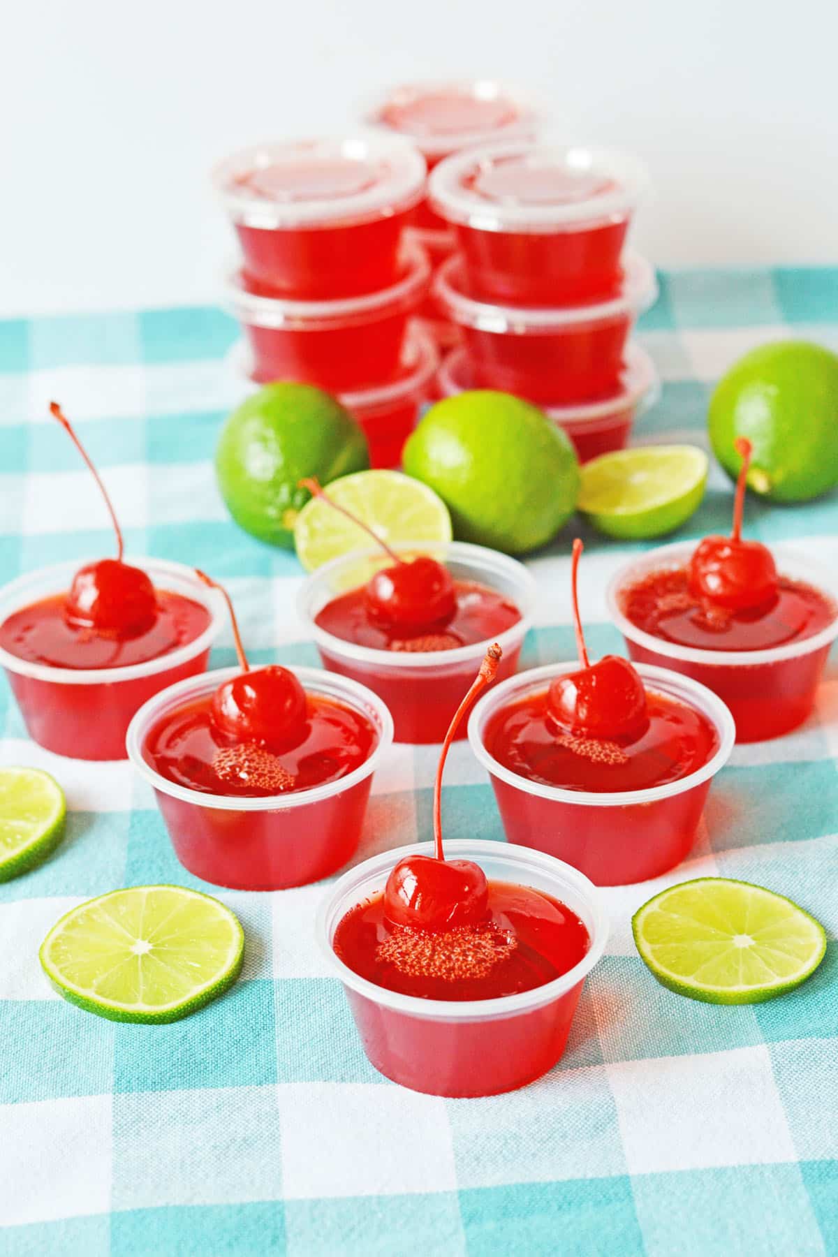 Aligned cherry limeade jello shots in blue checkered table cloth with lime slices