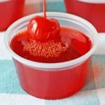 A cherry limeade Jell-O shot in a cup with cherry on top