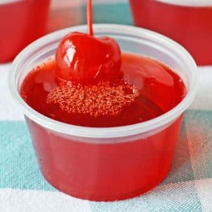 A cherry limeade Jell-O shot in a cup with cherry on top