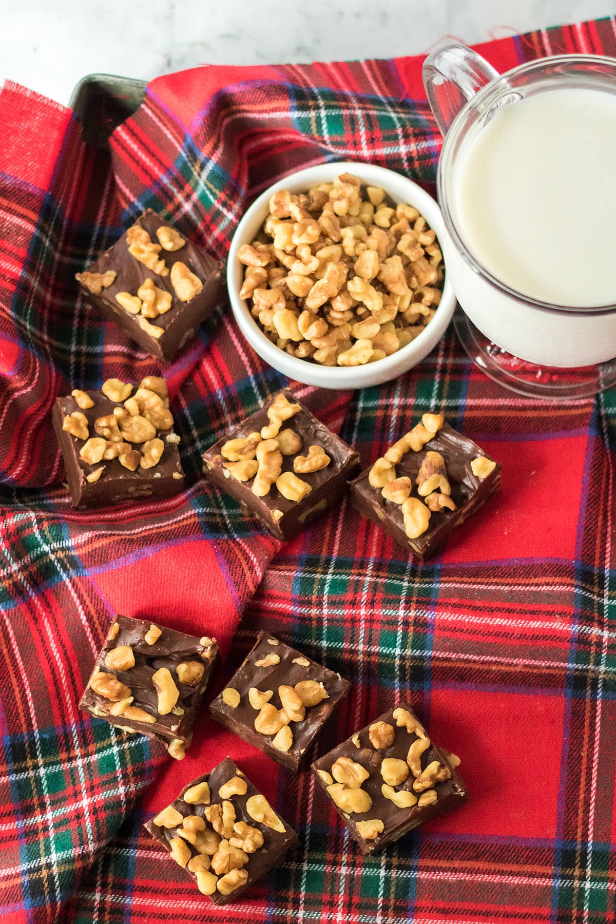 Vibrant tablecloth with a glass of milk, a bowl of walnuts, and pieces of Coca-Cola fudge