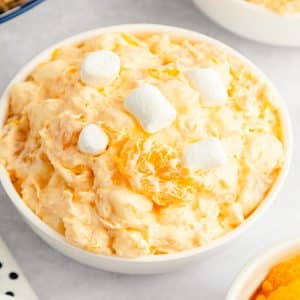 Orange fluff salad in serving bowl with white mallows on top
