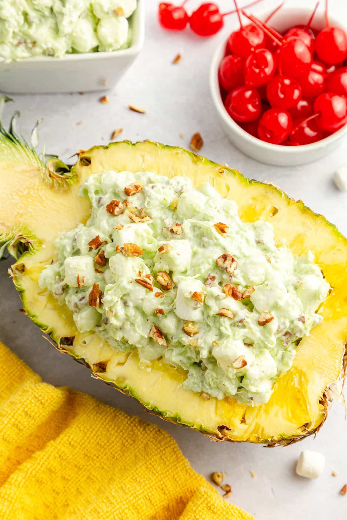 Chopped pecans are sprinkled on top of a half-cut pineapple with Watergate salad