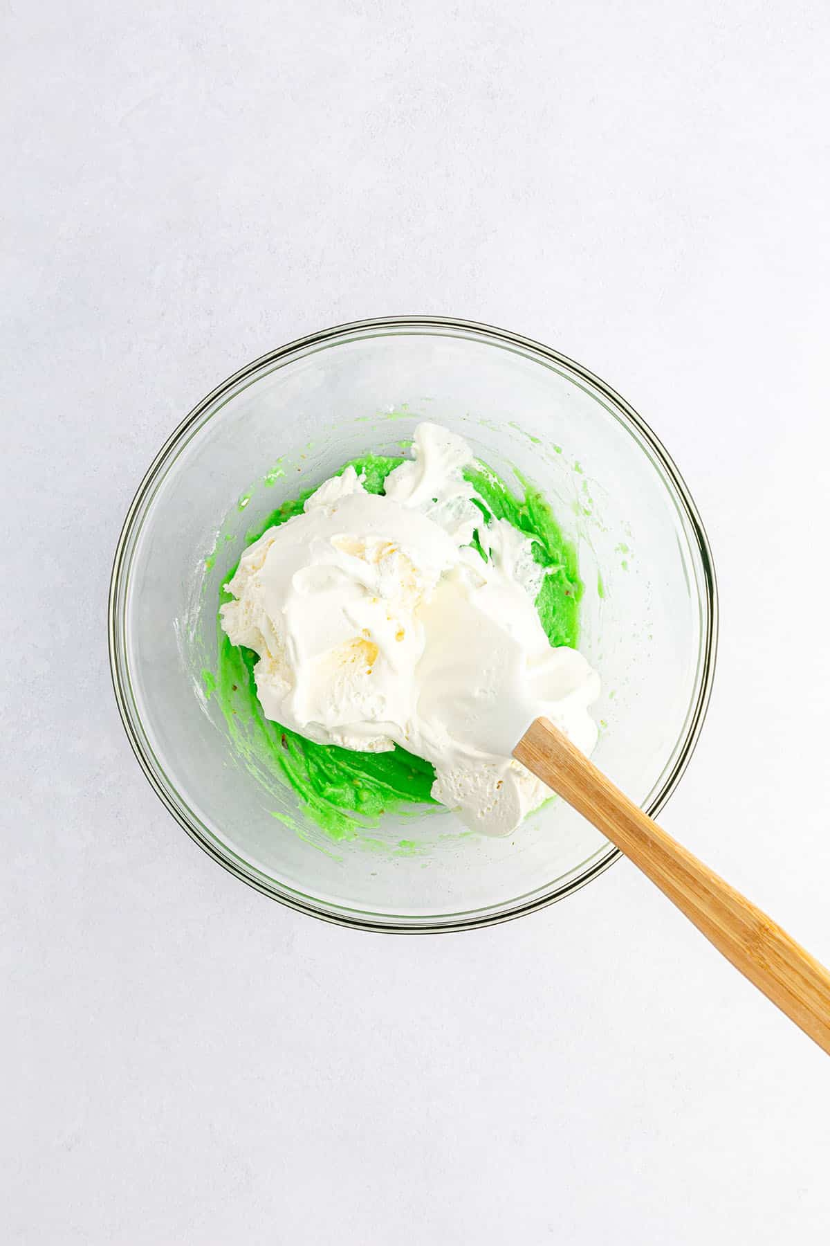 Green pudding mixture with whipped cream on top and spatula