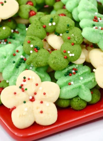 German spritz cookies on a red plate with green and white sprinkles.