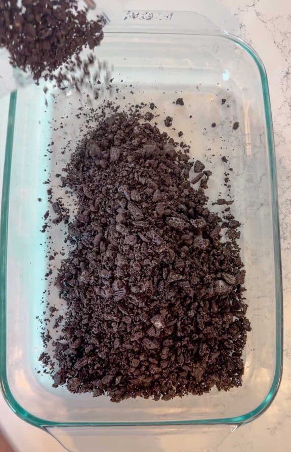 crushed Oreos being places in bottom of glass pan